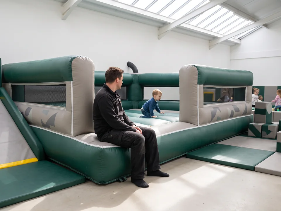 Low-walled toddler bouncer beside a toddler area, a parent seated at the edge