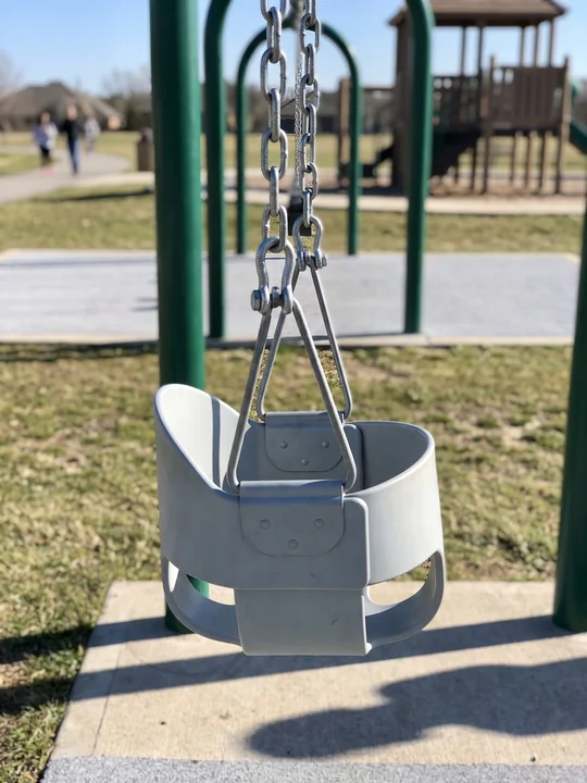 A grey full-bucket toddler swing seat hanging still on its chains