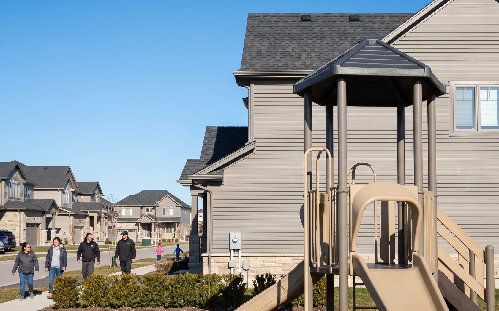 Side of a home in warm grey siding, charcoal roof and sand stone base, with a play structure beside it in the same three colors