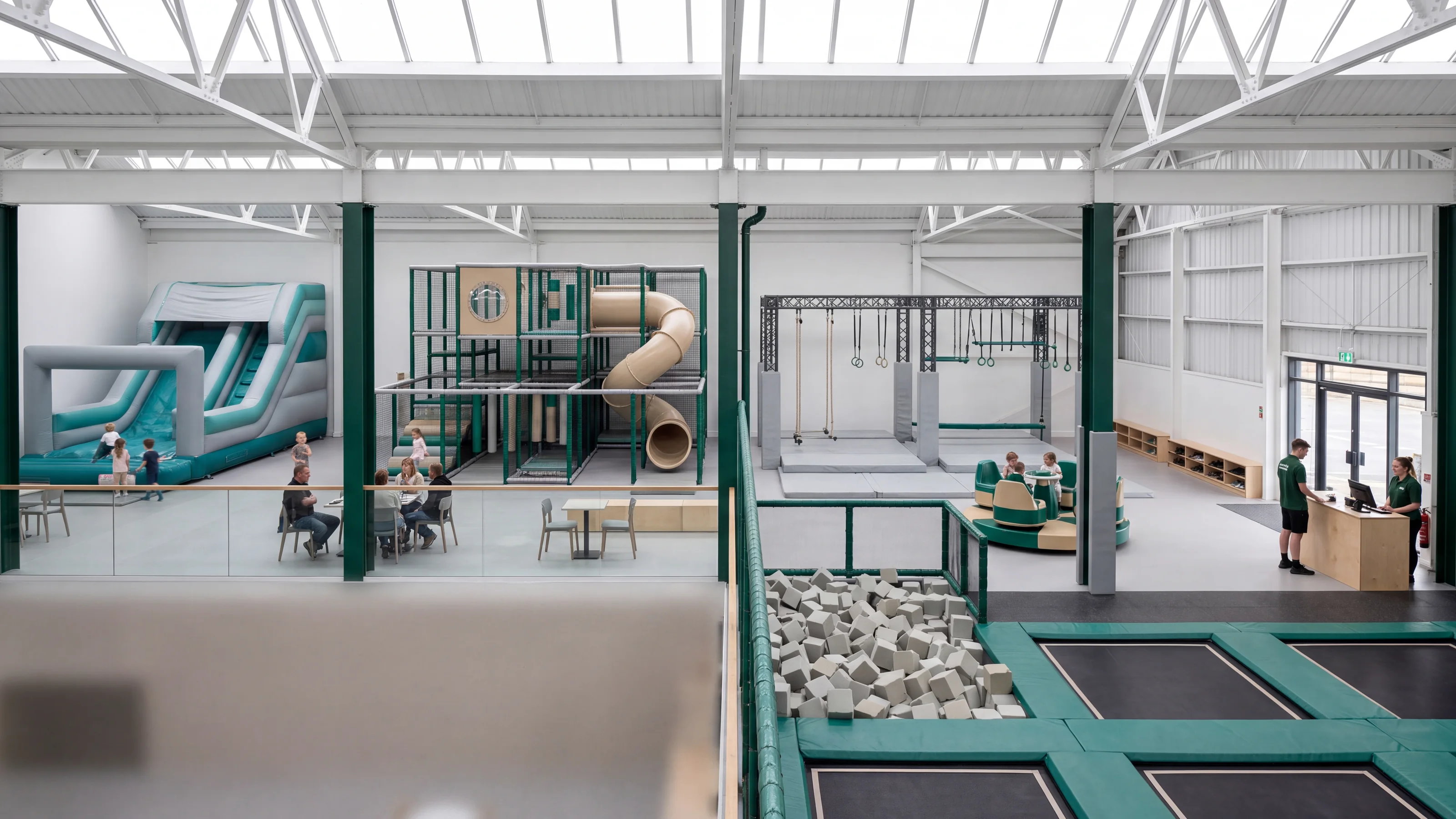 A skylit family entertainment center floor with an inflatable beside a soft play structure and a trampoline court