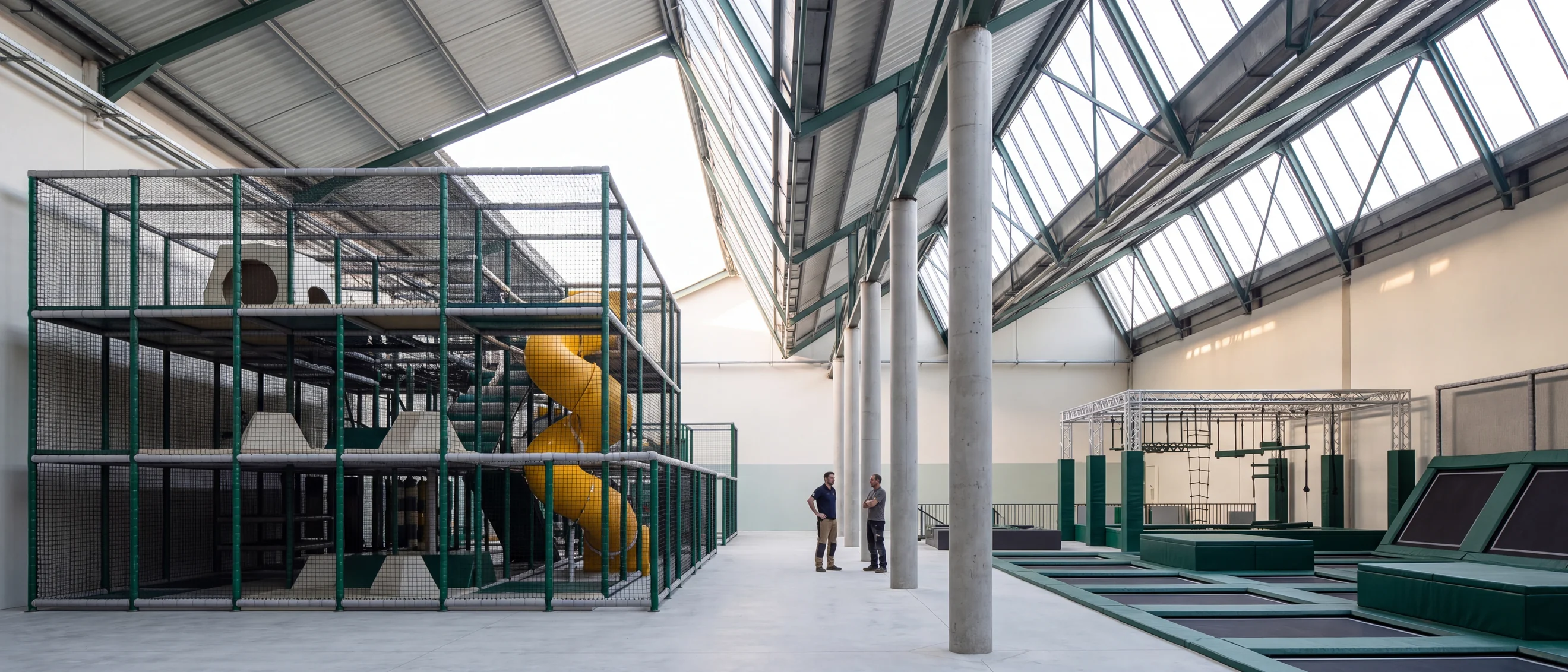 Indoor family entertainment center seen in section: a three-level soft play structure, a row of columns and a trampoline court under skylights