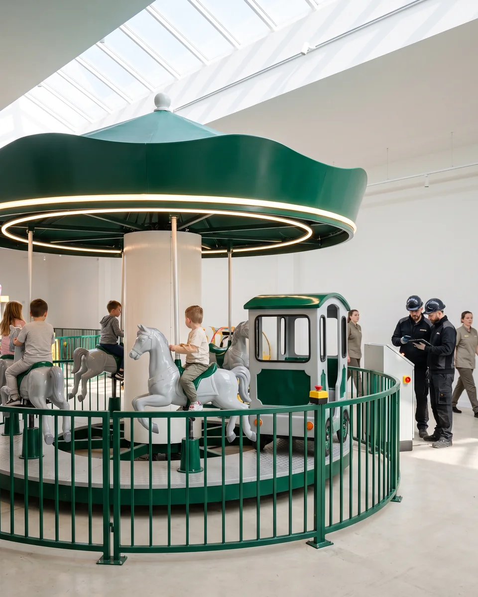 New small electric carousel with an evergreen canopy and warm-white lights in a skylit venue