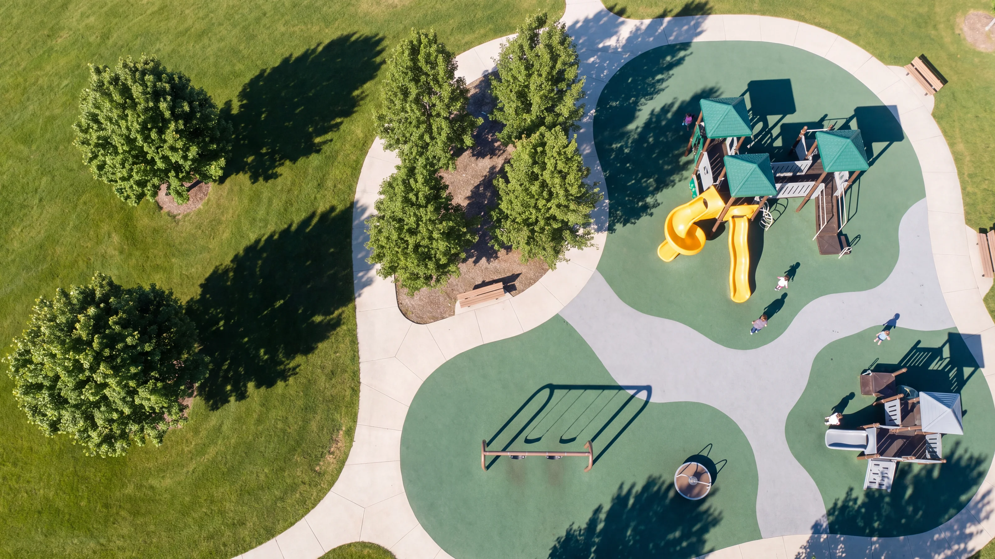 A straight-down view of a park playground with evergreen and grey rubber surfacing zones