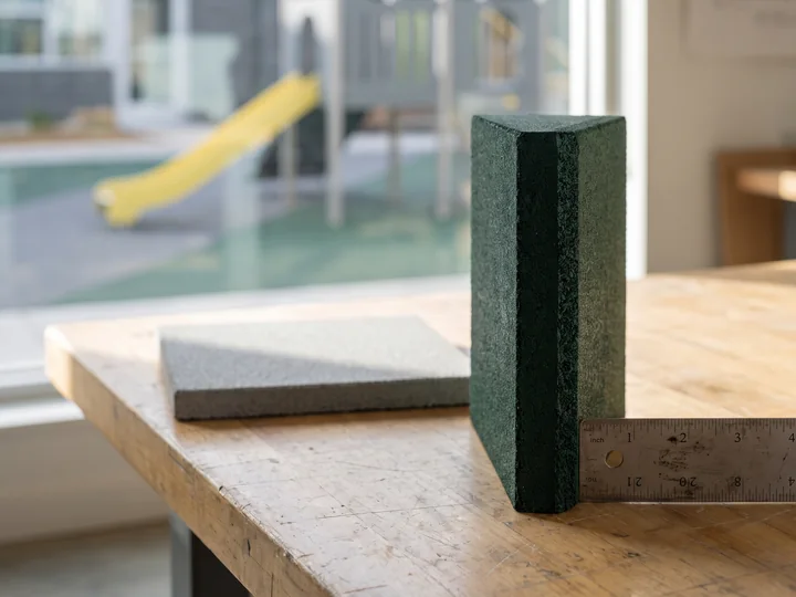 A cut rubber surfacing tile standing beside a steel ruler, its thickness plainly visible