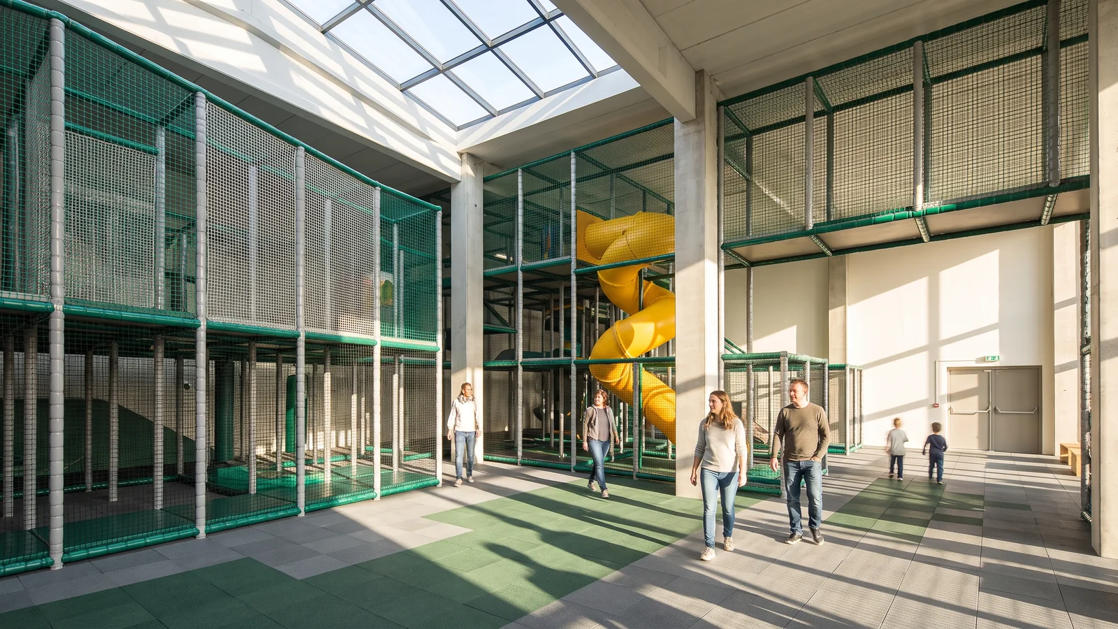 A skylit indoor venue with a multi-level soft play structure between columns