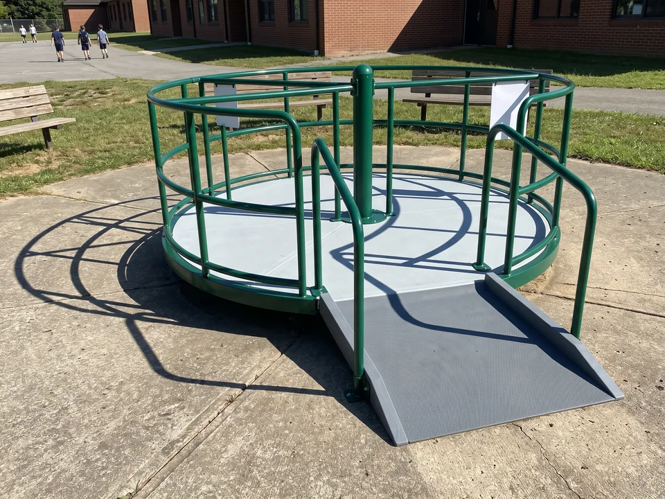 A ramped inclusive spinner standing on hard paving with a short ramp up to its solid deck