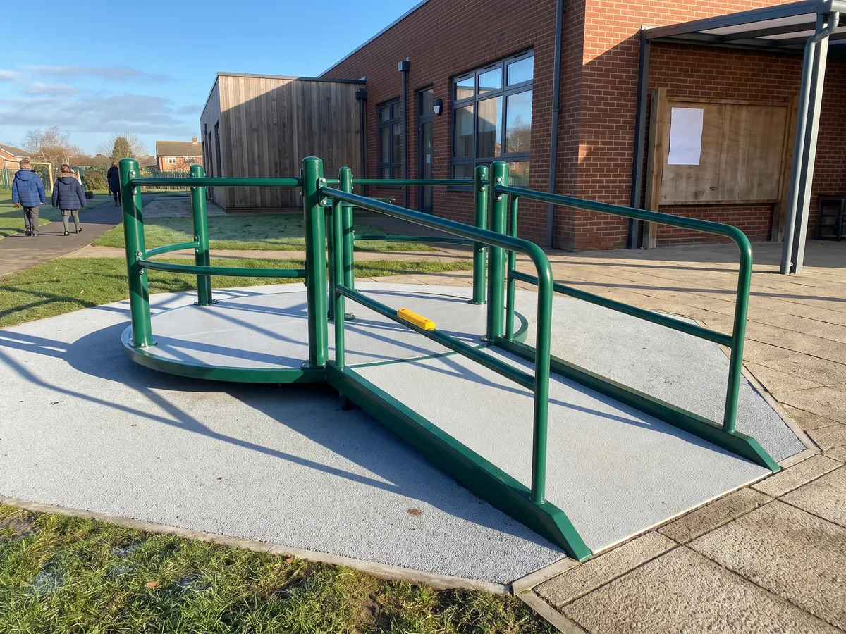 A ramped inclusive spinner at the edge of a paved school yard, the ramp meeting the yard paving
