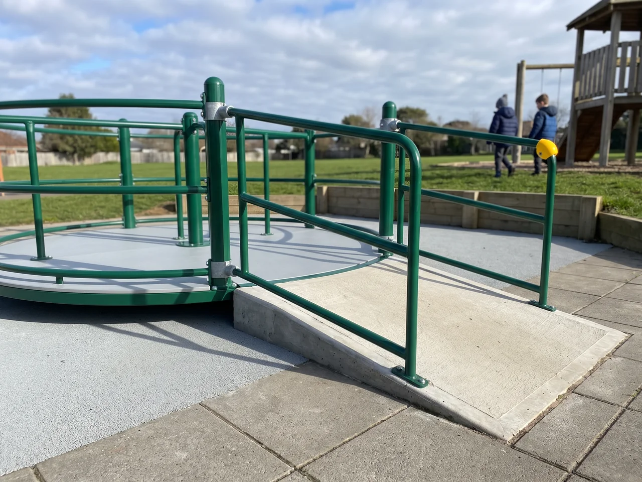 The same solid-deck inclusive spinner standing on paving with a ramp up from the path