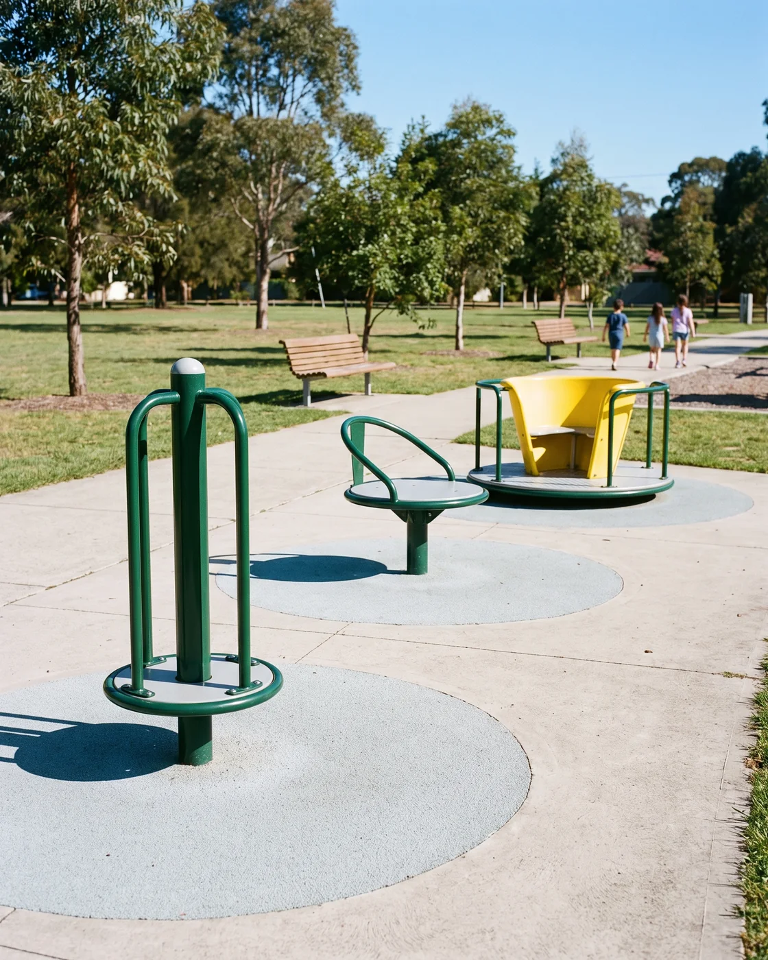 A row of a spin pole, an evergreen spin seat and a yellow spin cup along a park path
