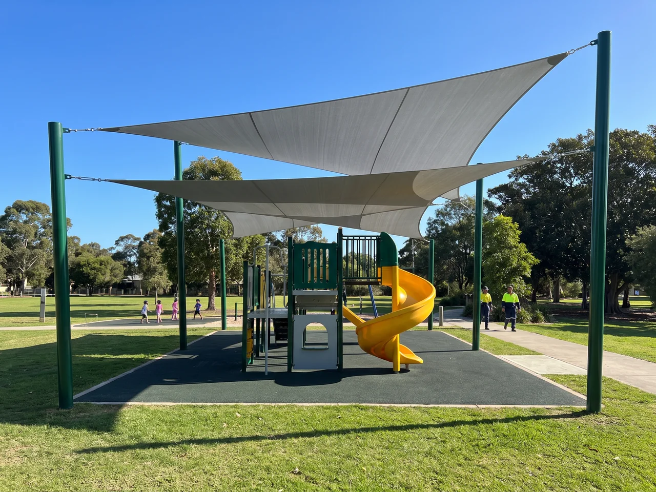 Two tension shade sails layered at different heights on their own evergreen posts over a play structure