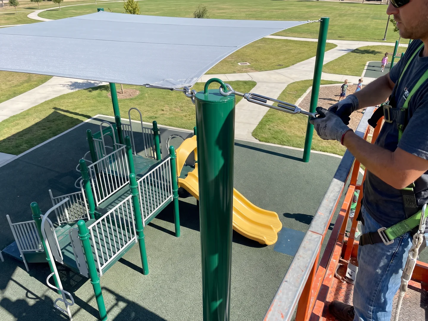Installer on a lift tensioning a turnbuckle at the top of a shade post