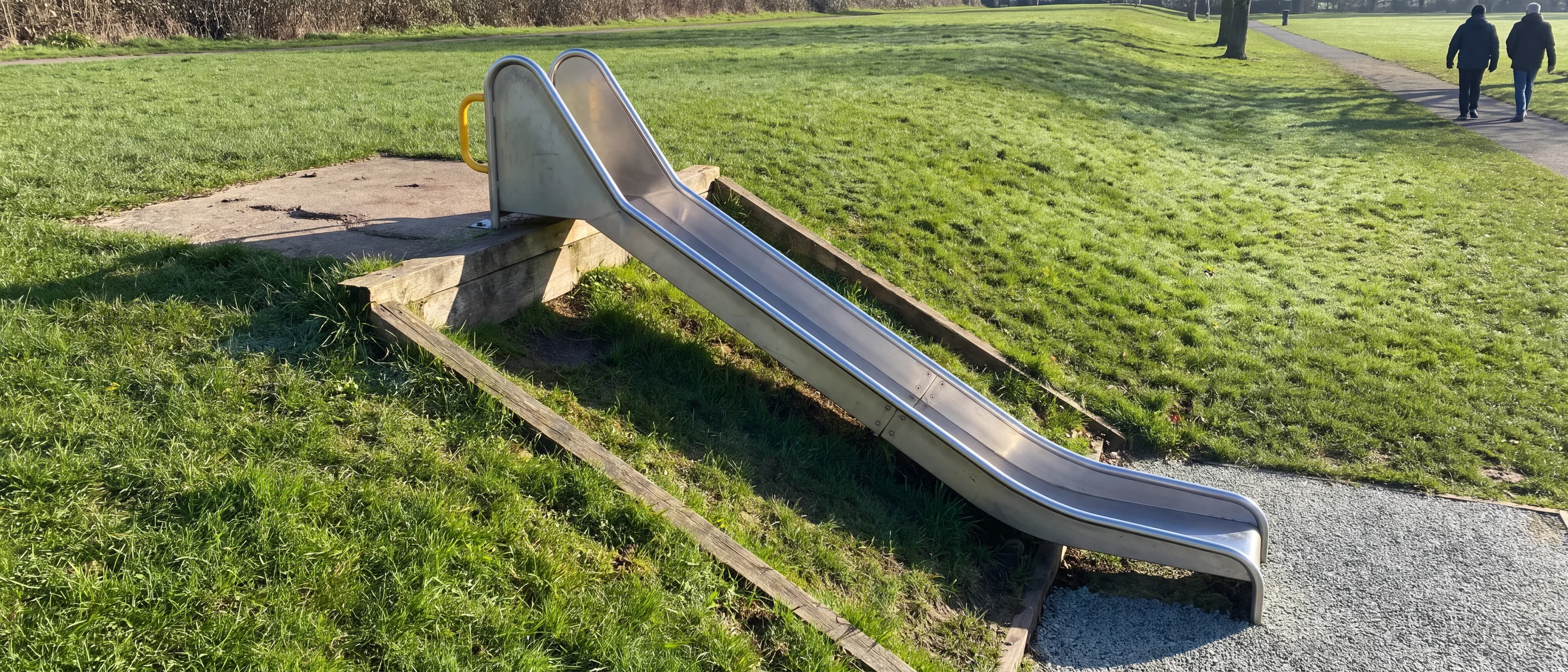 A stainless steel embankment slide running down a grassy park bank