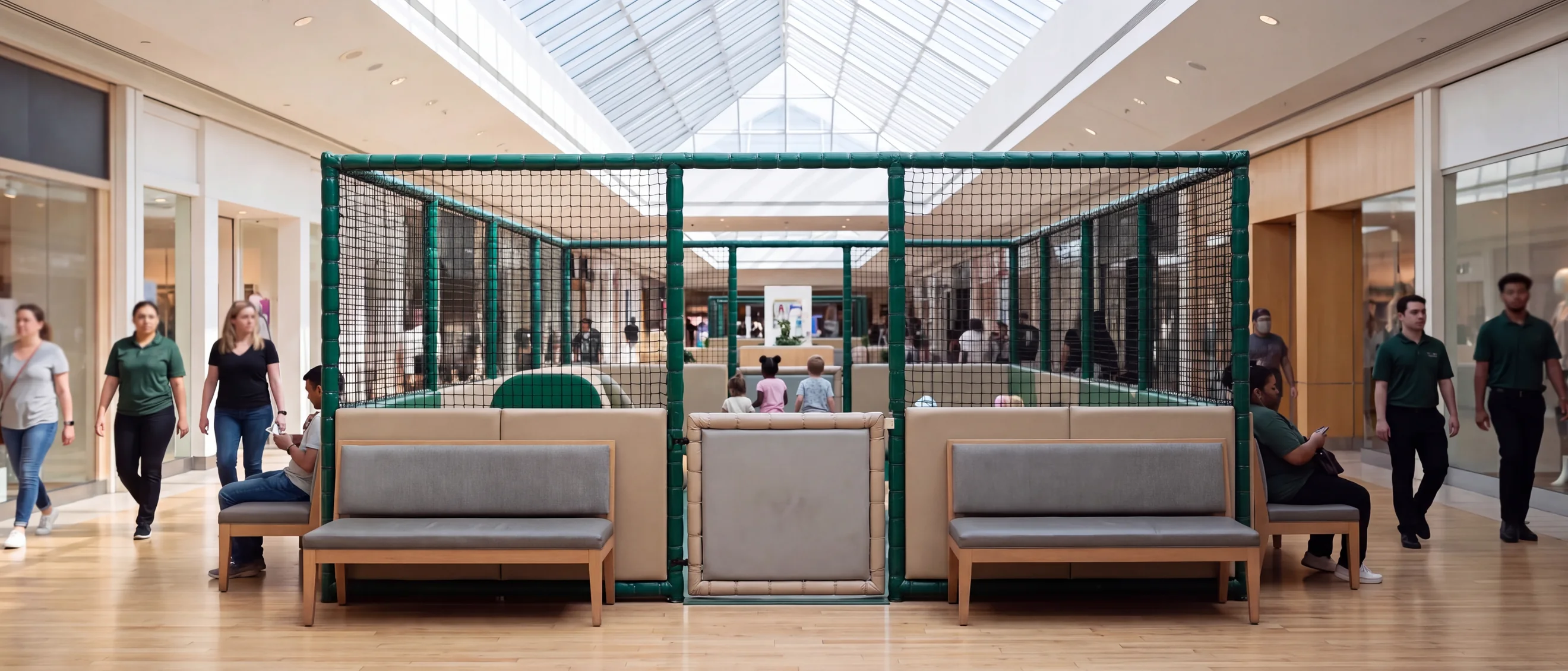 Enclosed soft play zone under a mall atrium skylight with shoppers passing on every side