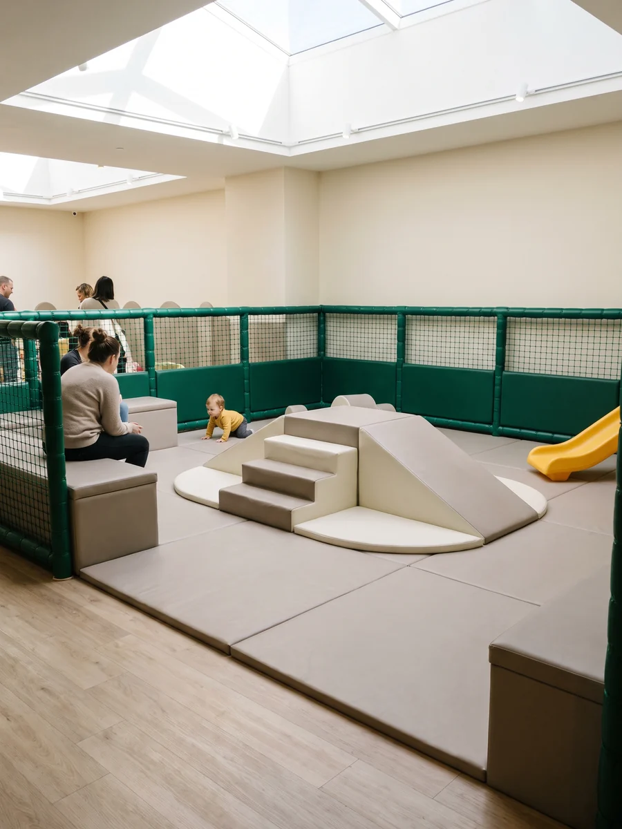 Toddler soft play zone with low padded pieces beside parent seating