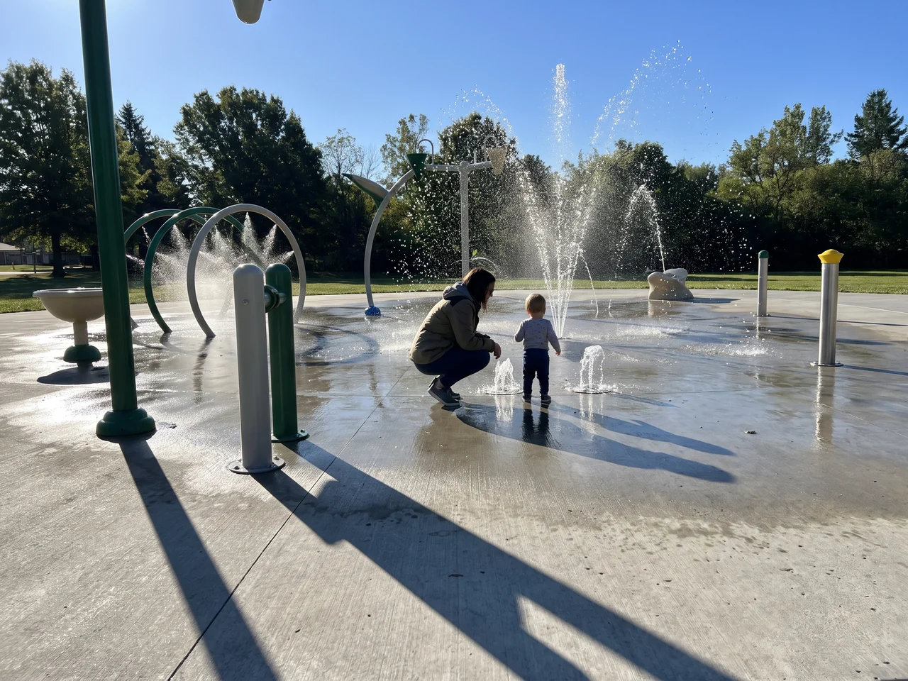 A toddler zone with low ground sprays, a small child and a crouching parent in the distance