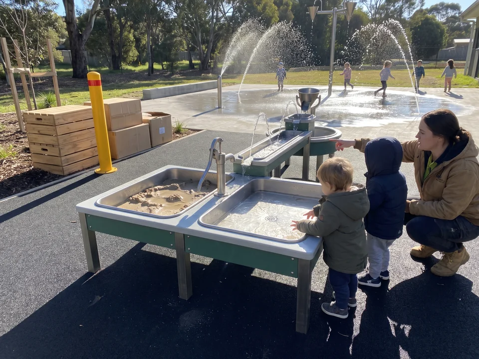 A child care center yard with a sand and water play table standing on rubber surfacing