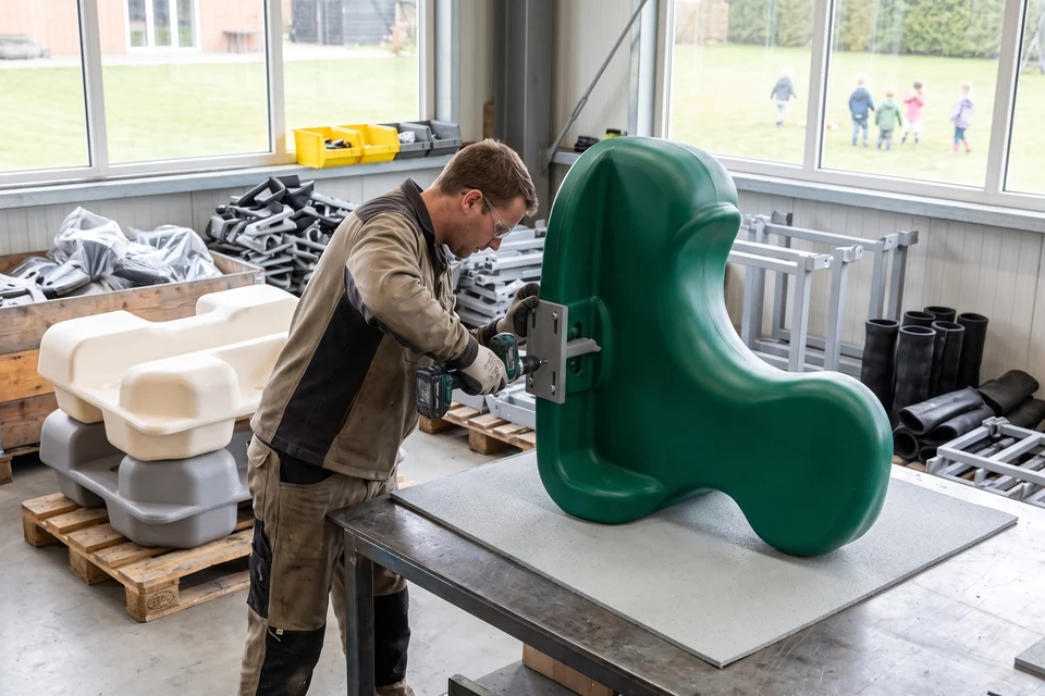 A worker drilling a fixing hole in a rotomolded spring rider body during trimming and drilling