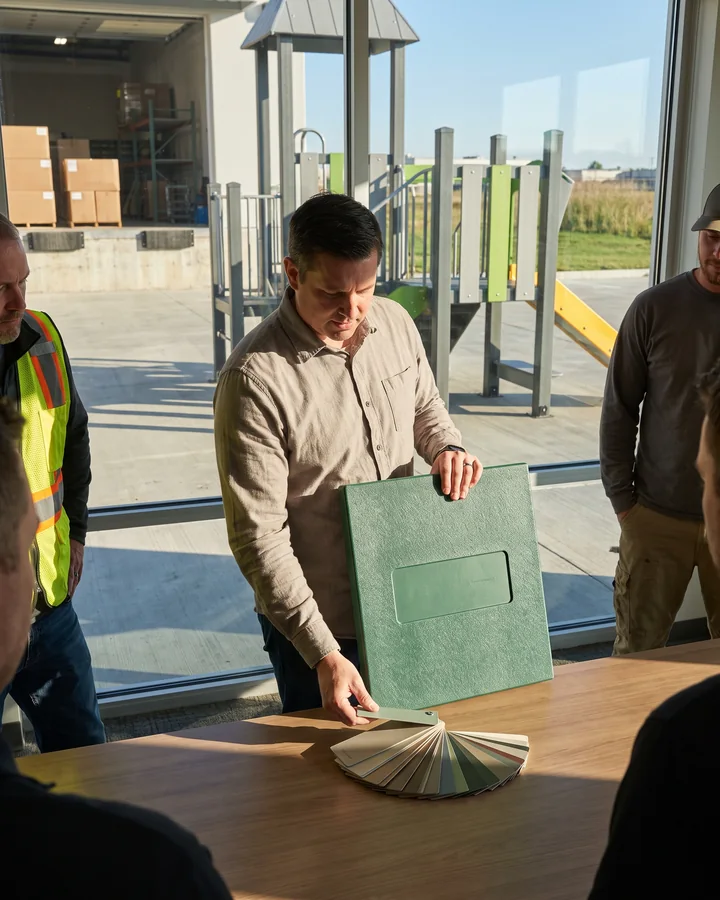 A play brand's product manager compares an HDPE sample panel with color chips at a meeting table